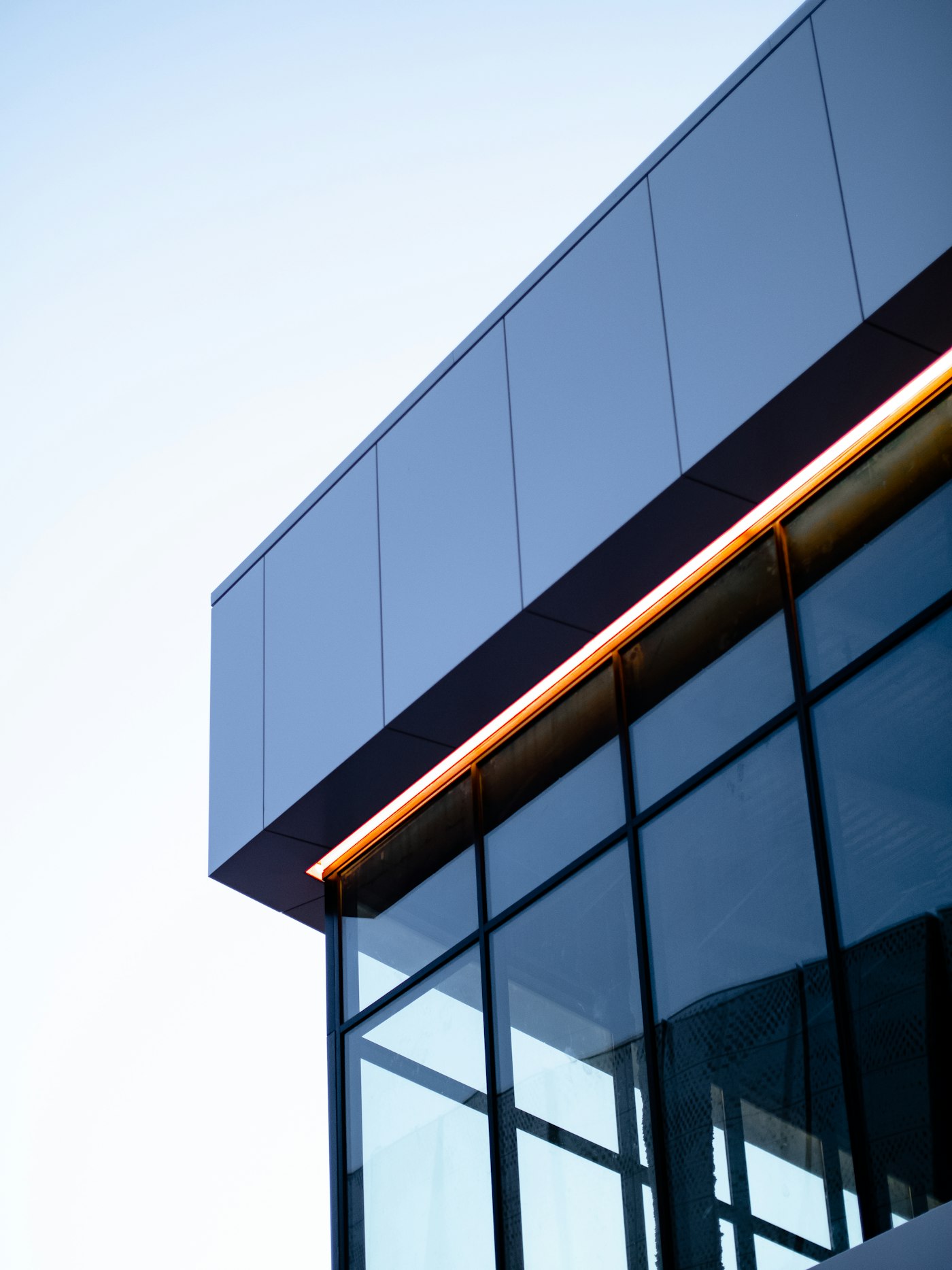 Moderne Architektur aus Glas und Stahl mit warmem Lichtband vor klarem Himmel
